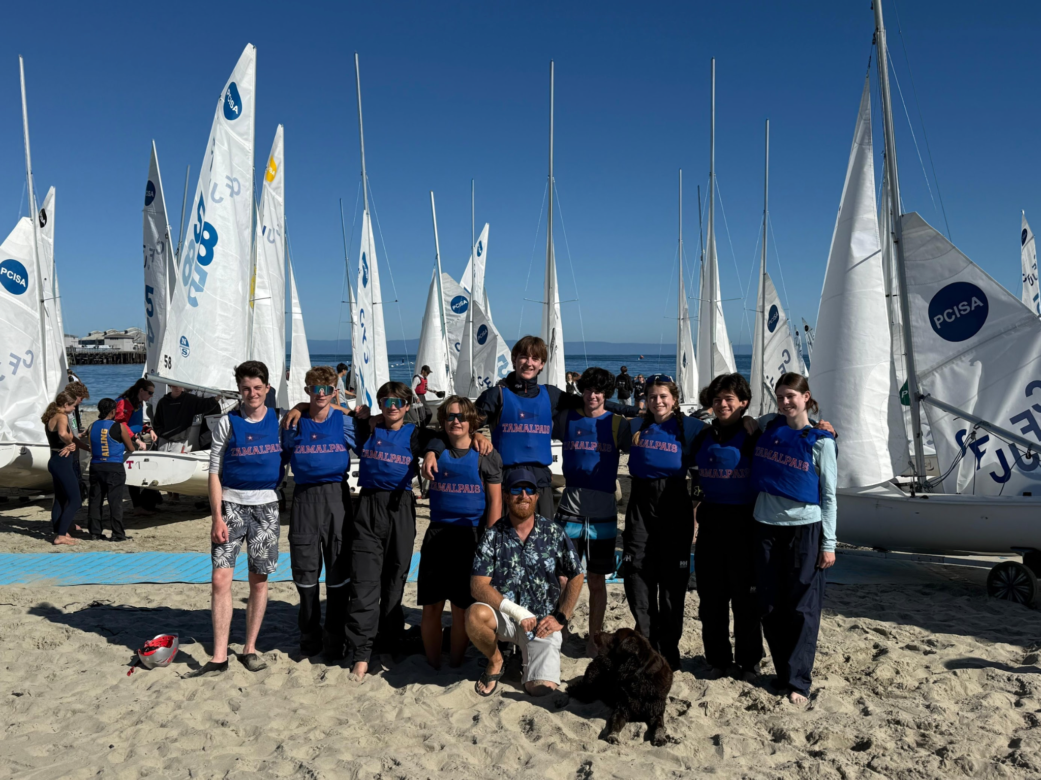 Tam High Sailing team standing together at a regatta with FJ sailboats behind them
